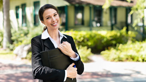 Smiling Realtor holding Padfolio in front of Home
